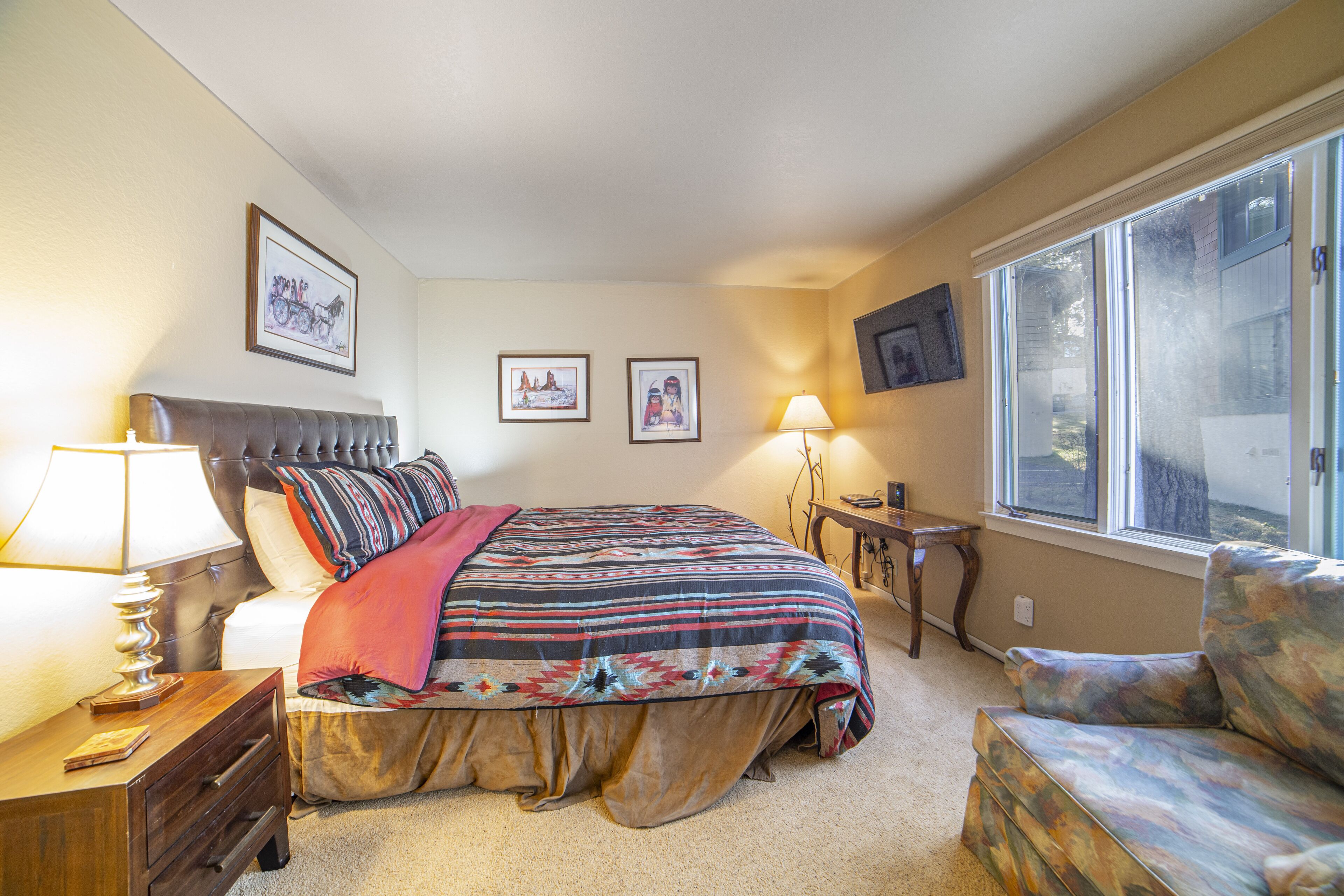 A bedroom with a bed, bedside tables, a window, and wall-mounted artwork.