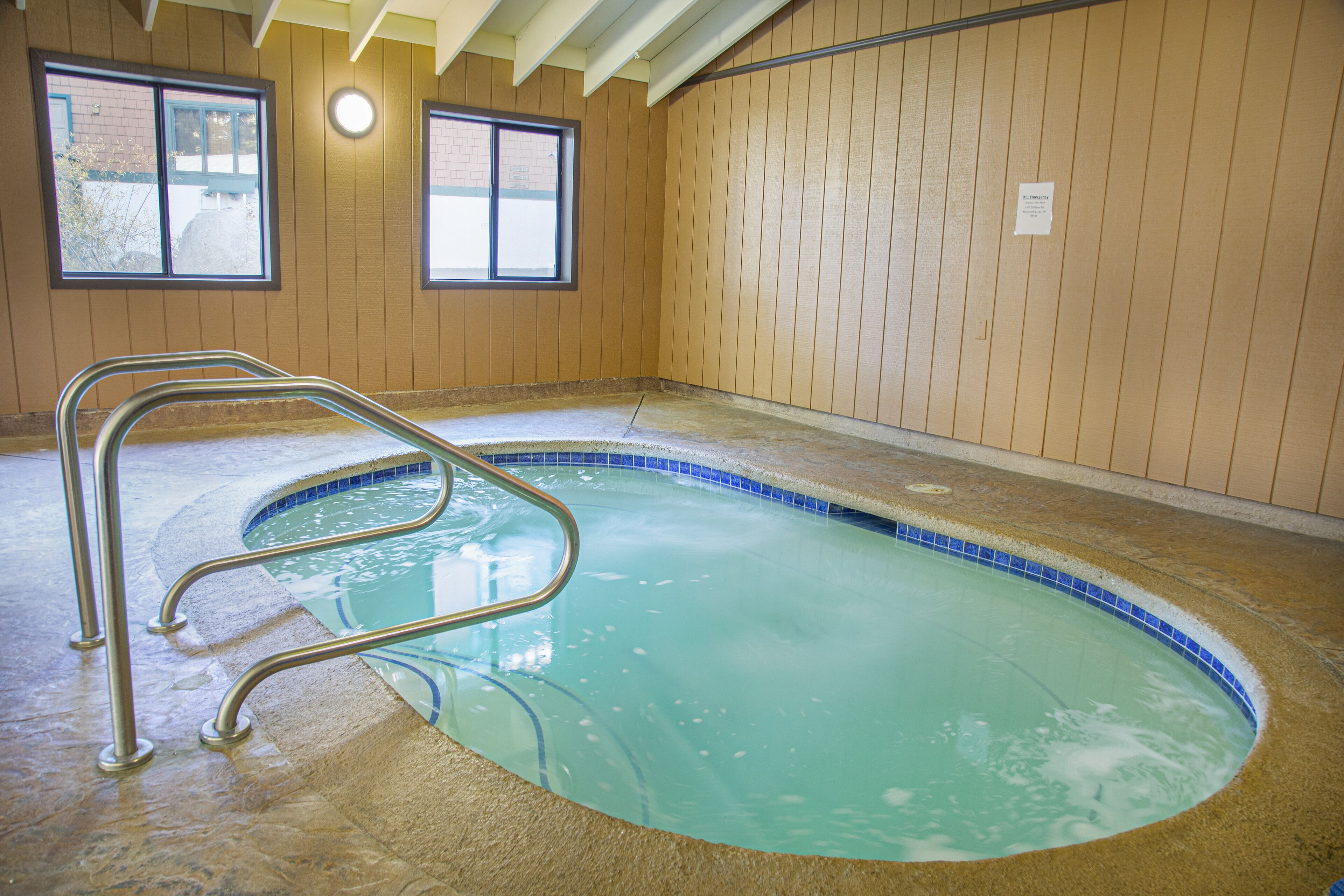 Una piscina interna con una scala in metallo, pareti in legno e finestre.