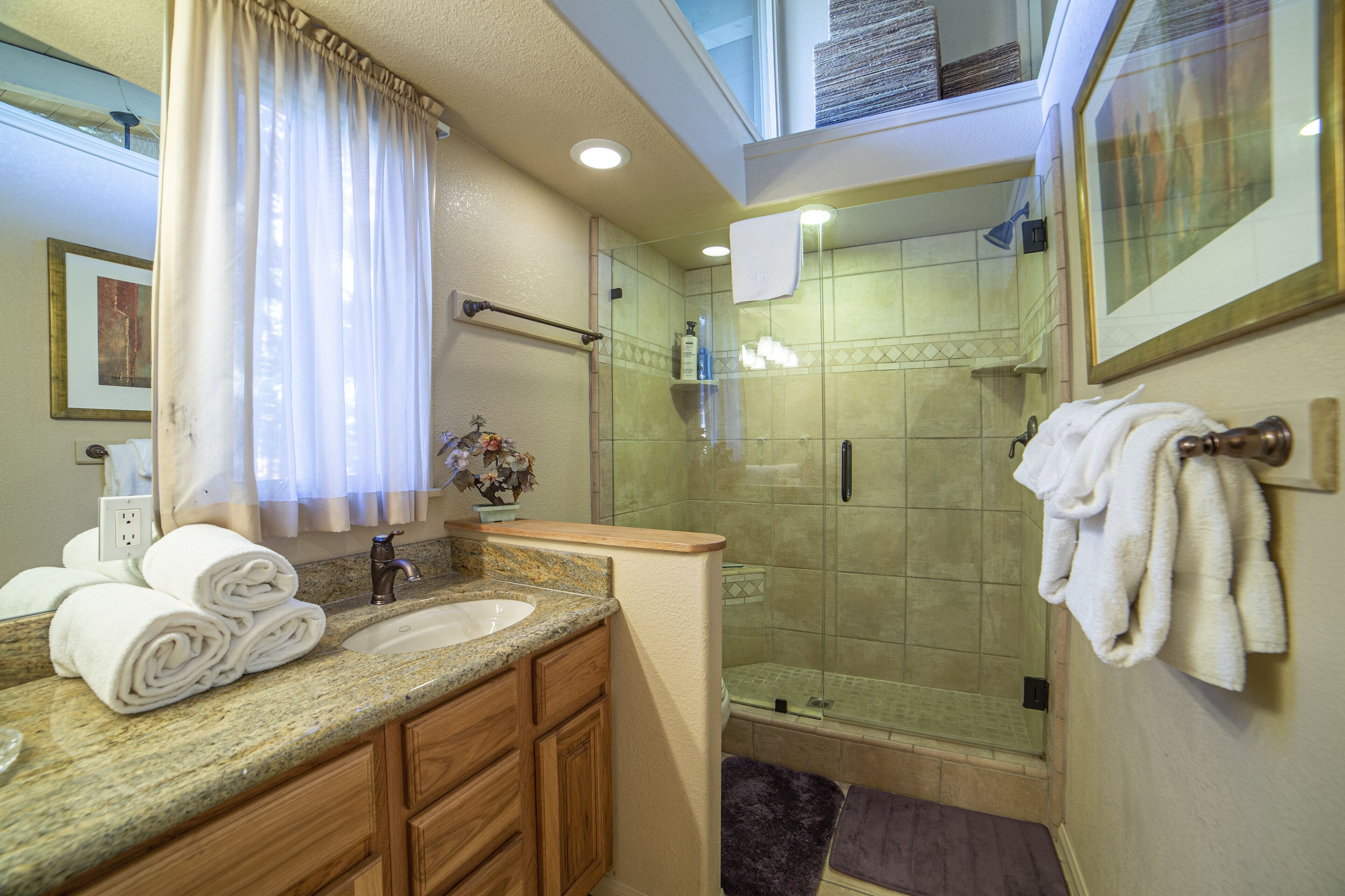 Une salle de bain dotée d’un comptoir en granit, d’armoires en bois, d’une cabine de douche en verre et d’un porte-serviettes.