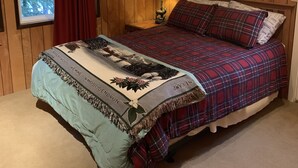 Ein Schlafzimmer mit Holzvertäfelung, einem Bett, einem Nachttisch, einer Lampe und einem Fenster mit Vorhängen.