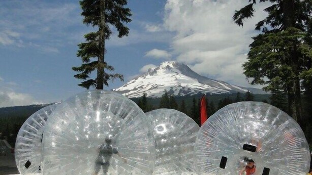 Drei transparente, kugelförmige Strukturen in einem Gewässer, mit einem Berg im Hintergrund.