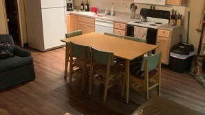 Eine kompakte Küche mit Holzausstattung, inklusive Kühlschrank, Mikrowelle und Herd. Es gibt einen Esstisch mit Stühlen, eine Couch und einen kleinen Couchtisch.
