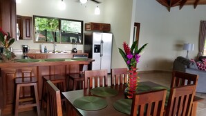 A modern kitchen with wooden cabinets, a built-in refrigerator, and a dining area with a wooden table and chairs. - Luxury Mountain Home with Ocean and Rain Forest Views.  Newly tiled pool! (Chontales)