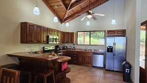 A spacious kitchen with wooden cabinets, a central island, a refrigerator, and a ceiling fan. - Luxury Mountain Home with Ocean and Rain Forest Views.  Newly tiled pool! (Chontales)