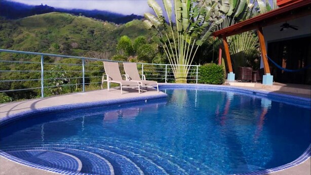 A swimming pool with two lounge chairs, surrounded by a metal railing, with a view of green hills in the background. - Luxury Mountain Home with Ocean and Rain Forest Views.  Newly tiled pool! (Chontales)