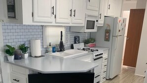 A modern kitchen with white cabinets, a built-in microwave, and a black TV on a lower shelf. - Your Home Away From Home FL Keys Paradise Rental (Key Largo)