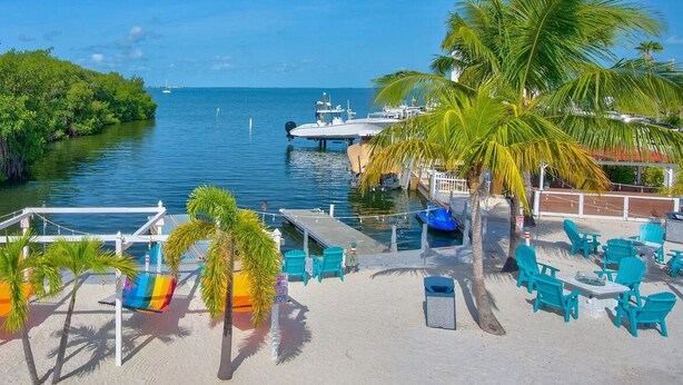 A beachside area with a dock, lounge chairs, and tables. - Your Home Away From Home FL Keys Paradise Rental (Key Largo)