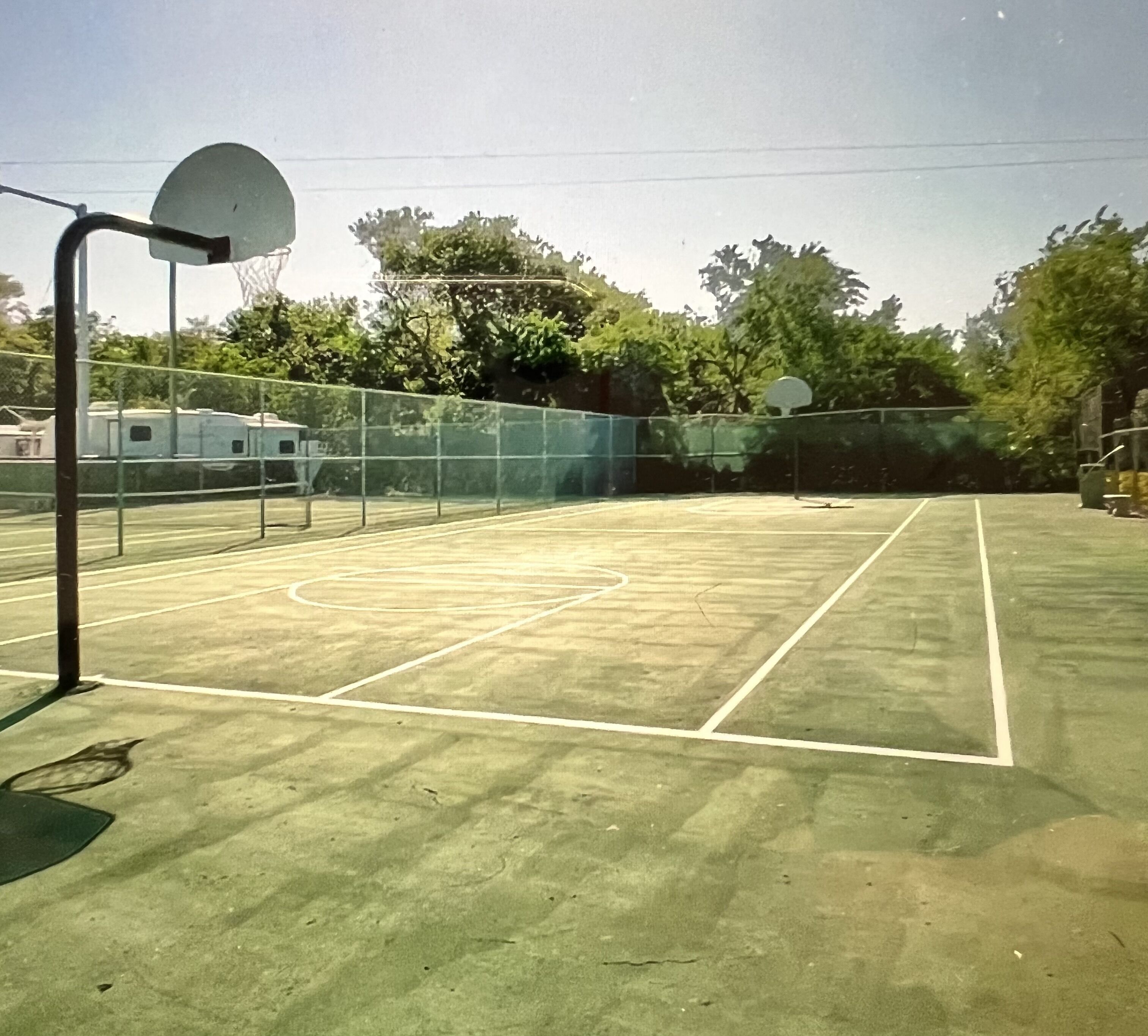 Een buitenbasketballbaan met een net, een ring en een hek.