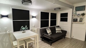 A compact living space with a white table and two chairs, a dark grey sofa with striped cushions, and a small shelf with decorative items. - Your Home Away From Home FL Keys Paradise Rental (Key Largo)