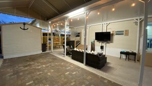 A covered outdoor area with a brick floor, seating arrangements, a television, and a fan. - Your Home Away From Home FL Keys Paradise Rental (Key Largo)