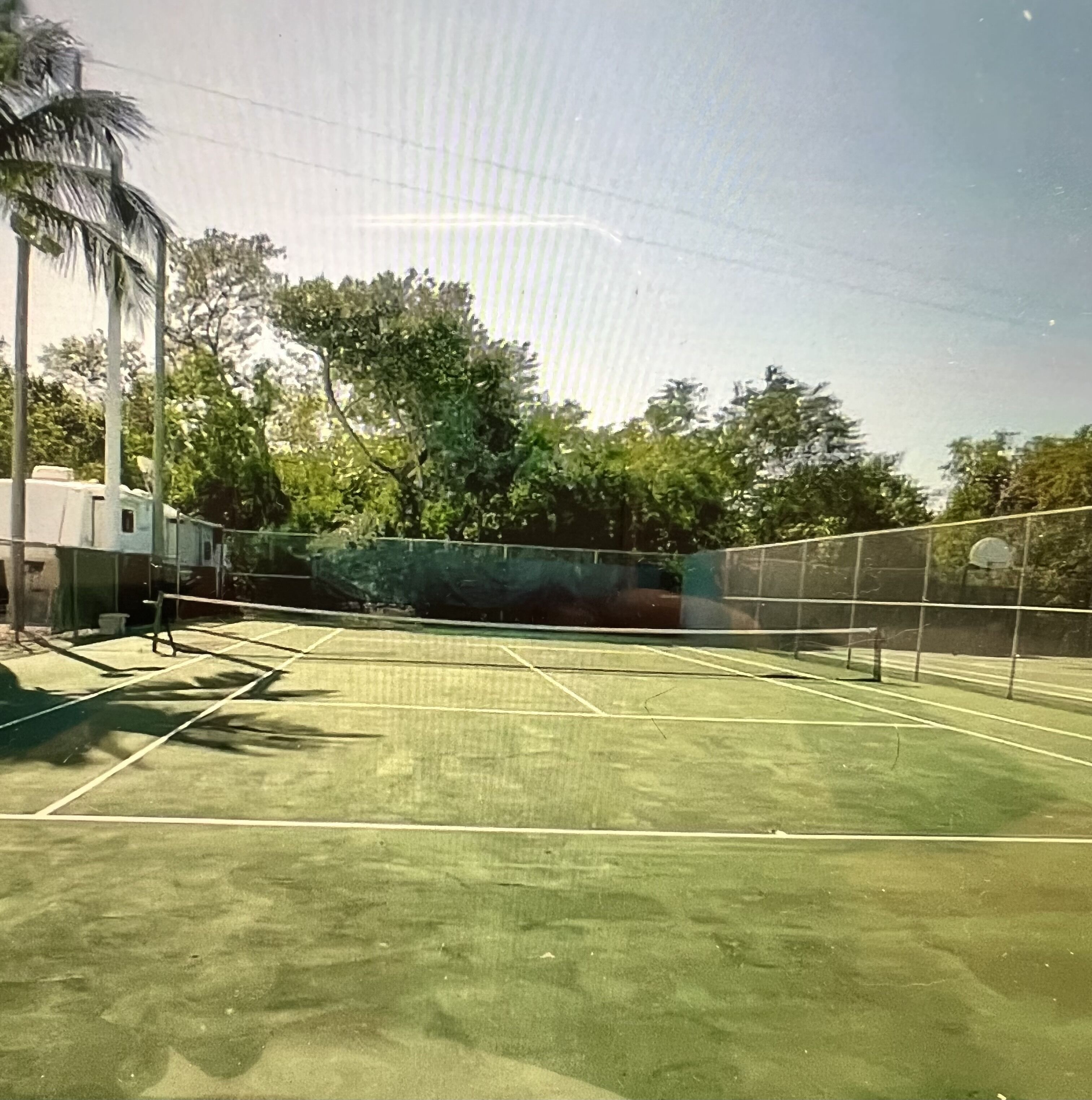 An outdoor tennis court with a net, surrounded by trees and a building.