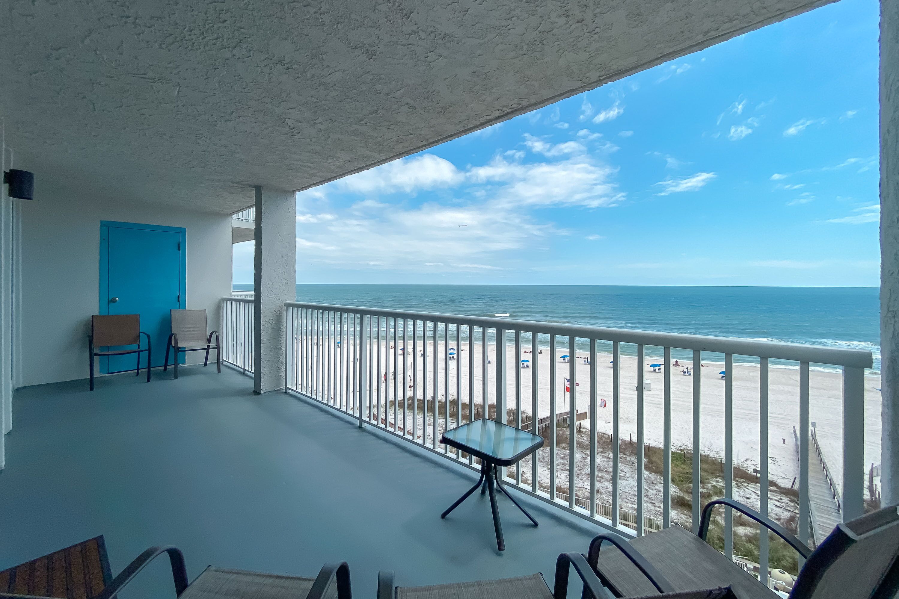 Un balcon donnant sur la plage, une porte bleue et deux chaises.