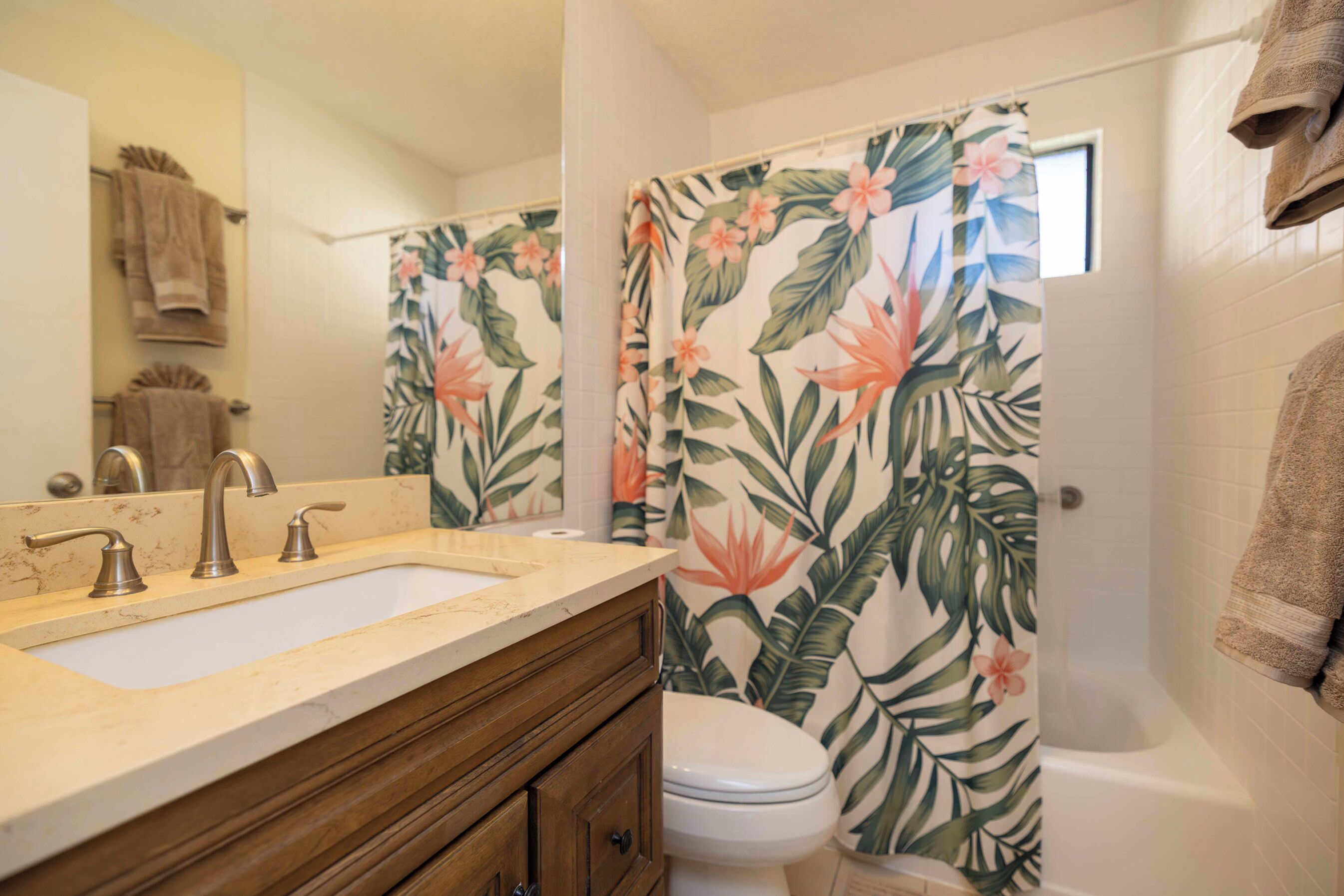 Une salle de bain avec un double lavabo, des toilettes et une douche agrémentée d’un rideau à motifs floraux.