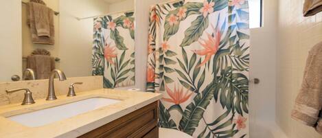 Une salle de bain avec un double lavabo, des toilettes et une douche agrémentée d’un rideau à motifs floraux.