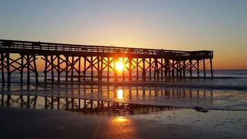 A pier extending into the water with the sun setting in the background.