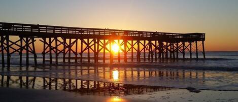 A pier extending into the water with the sun setting in the background.