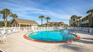 A swimming pool with lounge chairs and palm trees, surrounded by buildings.