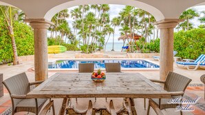 An outdoor pool area with a view of the beach, surrounded by palm trees and a thatched-roof structure. - The Best Beachfront villa w/pool, in a secure gated South Akumal community! (Akumal)