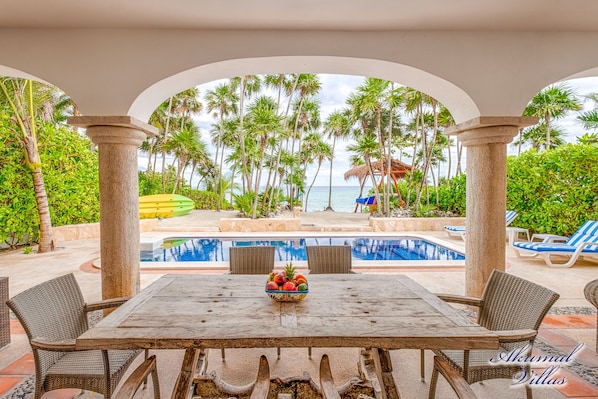 Un espace piscine extérieur avec vue sur la plage, entouré de palmiers et abrité par une structure à toit de chaume.