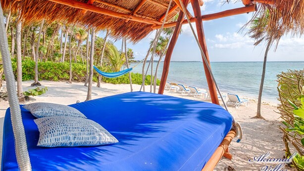 A hammock under a thatched roof, a bed with a blue mattress and pillows, and a beach with lounge chairs and palm trees. - The Best Beachfront villa w/pool, in a secure gated South Akumal community! (Akumal)