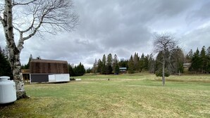 A grassy field with a large building and trees in the background.