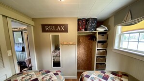 A bedroom with two beds, a closet with storage bins, a 'RELAX' sign, and a window with a view.
