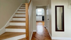 Een trap die leidt naar een keuken met witte kasten en een houten vloer.