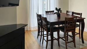Een eethoek met een tafel en stoelen, een televisie aan de muur en een raam met gordijnen.