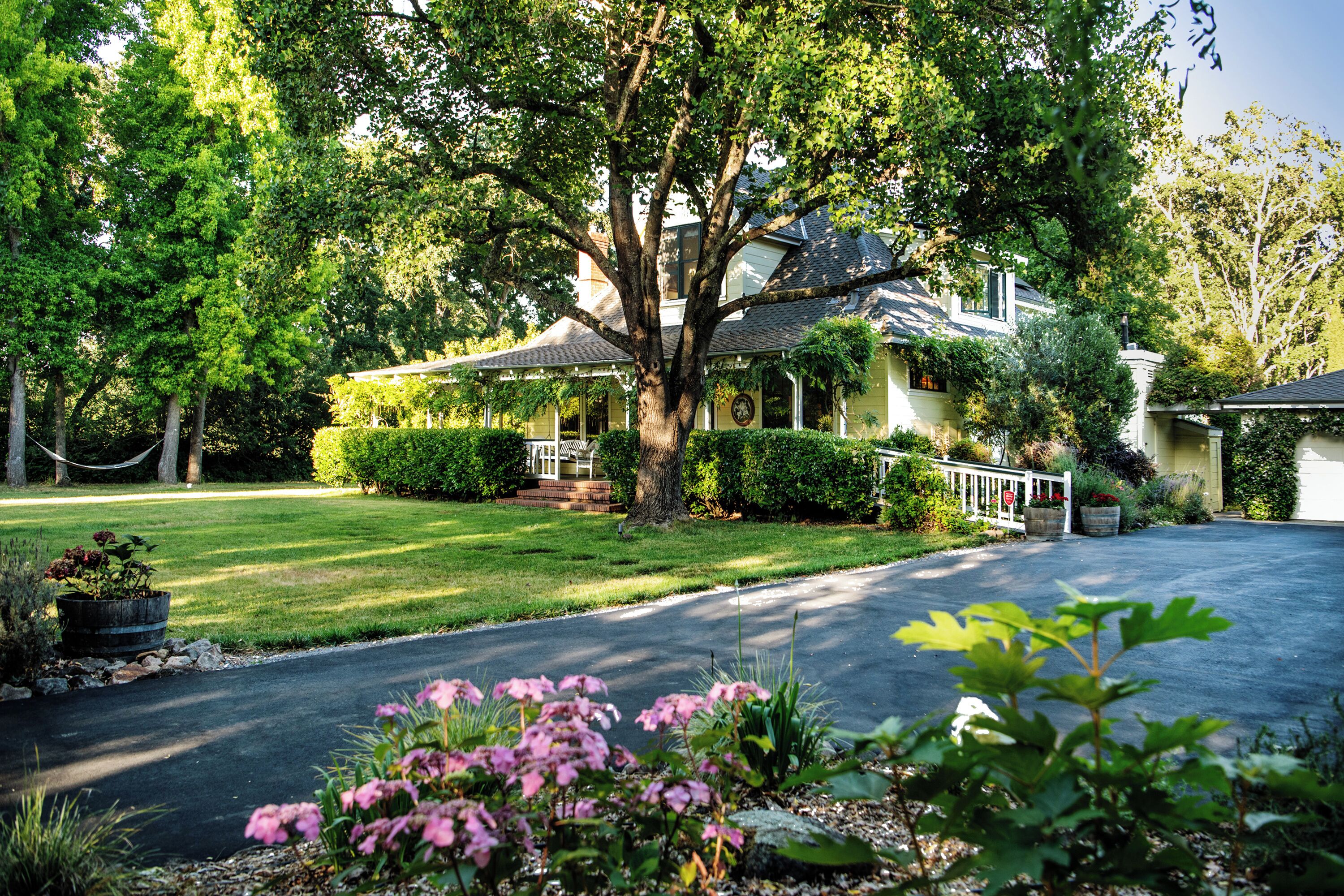 Vintage farmhouse with wraparound veranda amidst gardens and trees