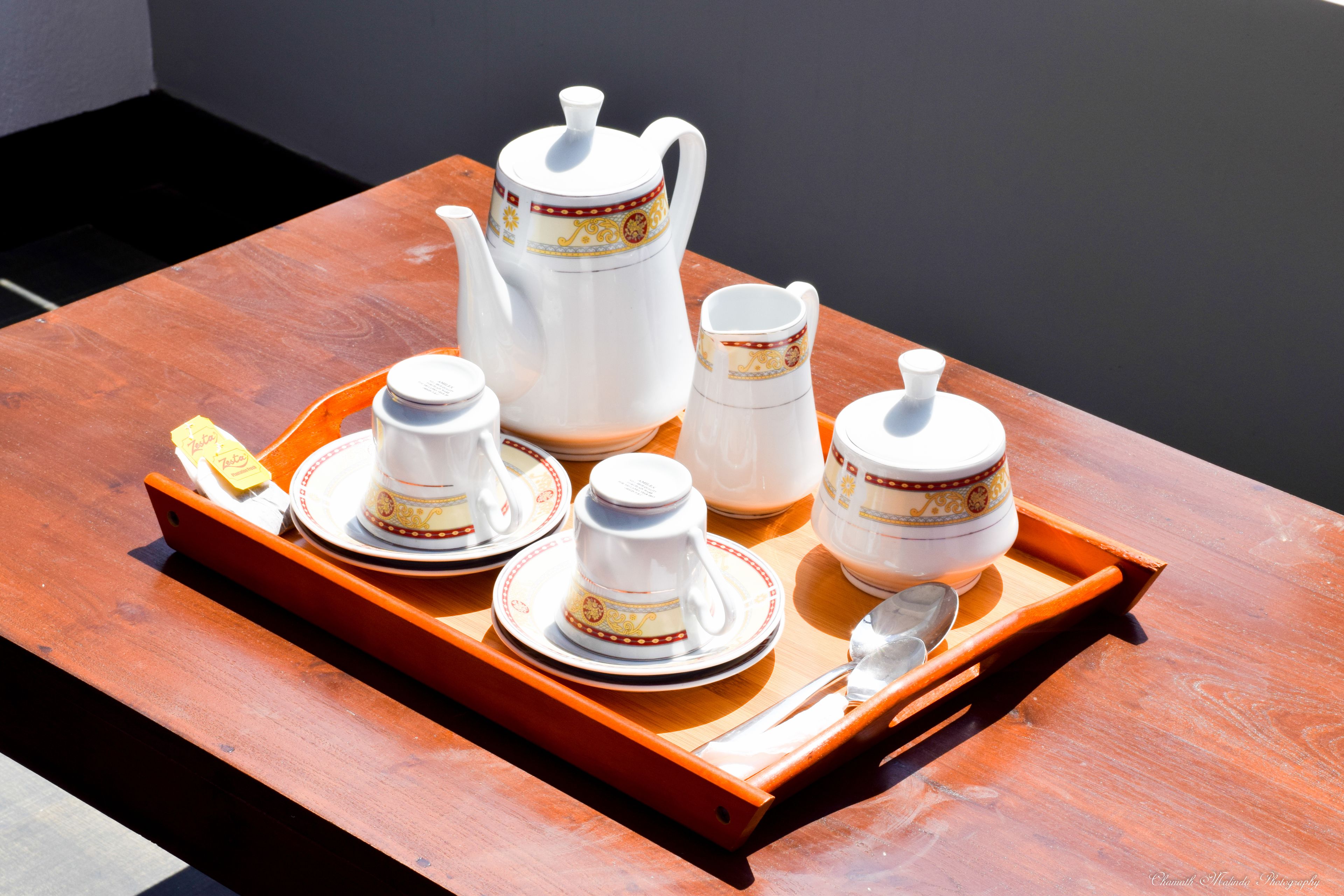 Un plateau avec une théière, des tasses, des soucoupes, un sucrier et une cuillère, posé sur une table en bois.