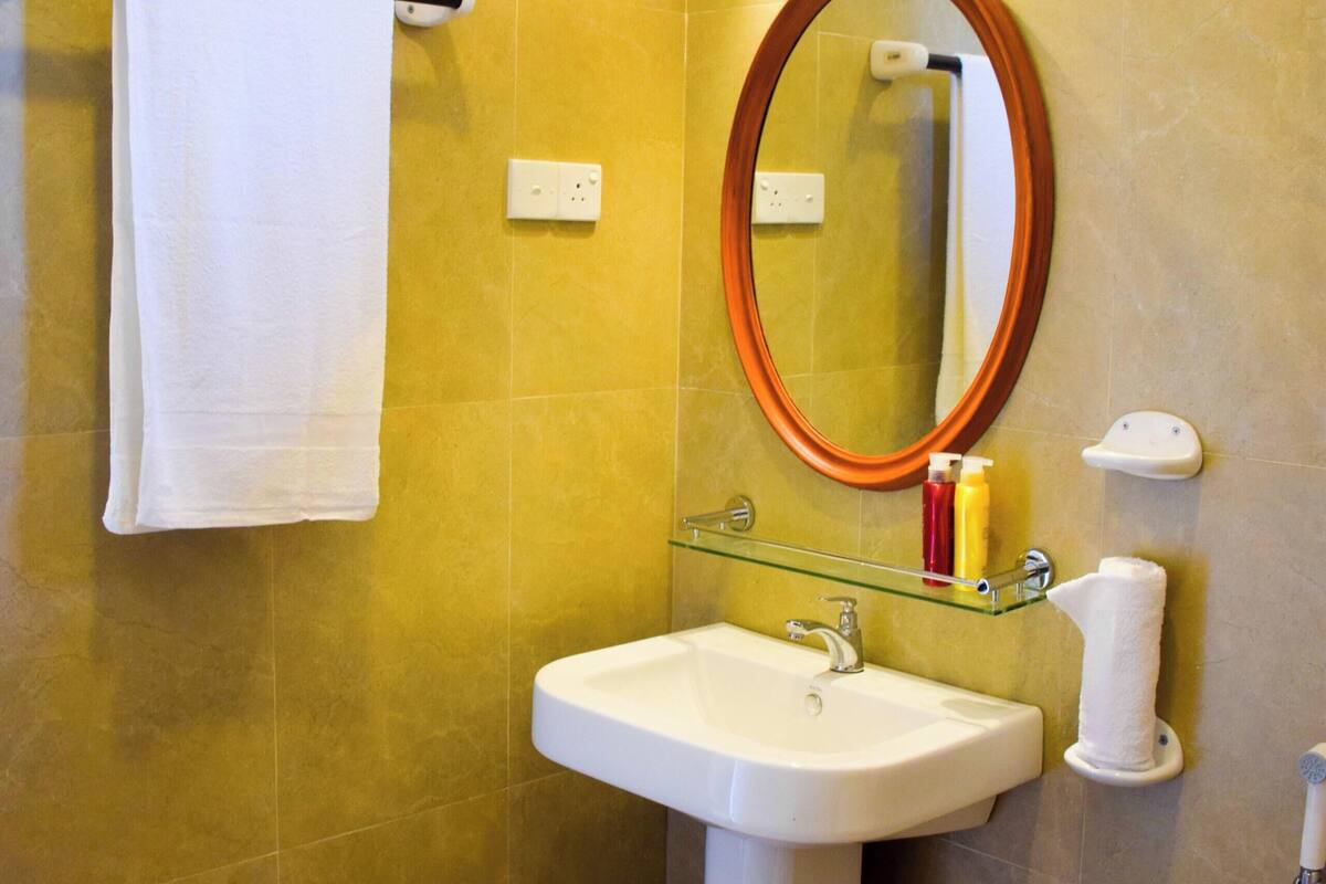 A bathroom with a sink, mirror, towel rack, and a glass shelf with toiletries.