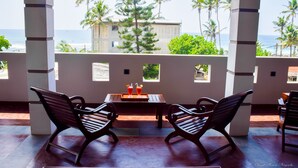 A covered outdoor seating area with two wooden benches and a table, overlooking a beach with palm trees and a building in the background. - Tenasi Beach Resort (Ahangama)