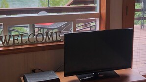 Een kamer met een houten bureau, een televisie en een raam met uitzicht op een bos en een waterpartij.