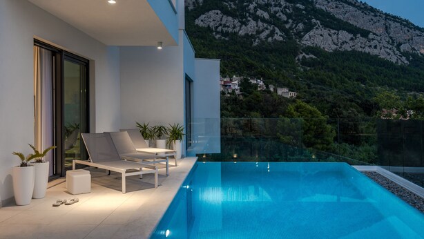 A modern outdoor pool area with lounge chairs and potted plants, overlooking a mountainous landscape. - Villa Zvizdan - authentic local experience (Makarska)
