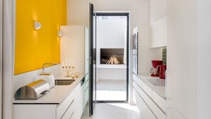 A modern kitchen with white cabinets, a yellow accent wall, and a view into the living area through an open door. - Villa Zvizdan - authentic local experience (Makarska)