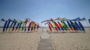 Une plage avec une promenade en bois menant à l’eau, bordée de drapeaux aux couleurs vives.