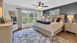 A bedroom with a bed, nightstands, a ceiling fan, a window with curtains, and a view of trees. - Family Friendly Lakeview Upper Vista in Sea Colony West (Bethany Beach)