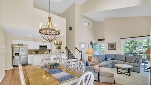 A spacious living area with a dining table, chairs, a chandelier, a sofa, and a staircase leading to another level. - Family Friendly Lakeview Upper Vista in Sea Colony West (Bethany Beach)