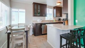 A modern kitchen with dark wooden cabinets, a white countertop, and a green accent wall. - 1 Bedroom Condo steps from Ocean and Bay (San Diego)
