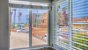 A room with a large window offering a view of a street and buildings, a wicker chair, and a window blind. - 1 Bedroom Condo steps from Ocean and Bay (San Diego)