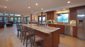 A spacious kitchen with a large island, wooden cabinets, stainless steel appliances, and large windows offering views of the outdoors.