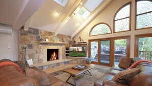 A spacious living room with a stone fireplace, leather sofas, and large windows offering views of the outdoors.