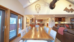 A spacious dining area with a wooden table and white chairs, a living room with a brown leather sofa, and a mounted animal head on the ceiling.