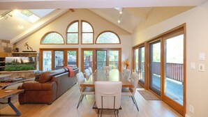A spacious dining area with a wooden table and white chairs, large arched windows, and a stone fireplace.