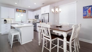 A modern kitchen with white cabinetry, a central island, and a dining area with white chairs.
