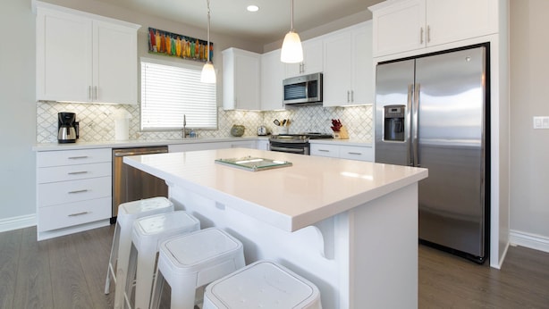 A modern kitchen with white cabinetry, a stainless steel refrigerator, and a central island with bar stools.