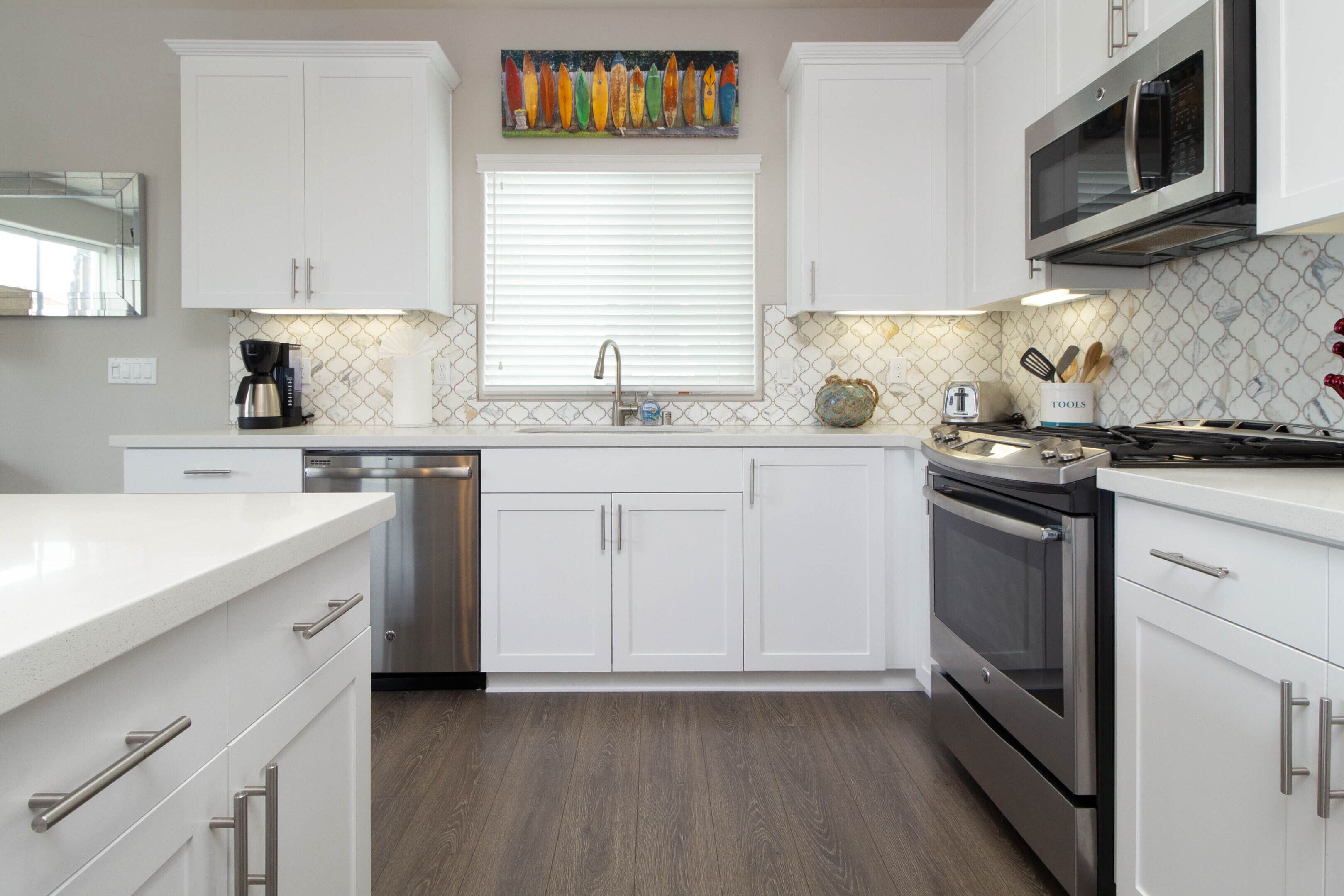 A modern kitchen with white cabinetry, stainless steel appliances, and a wooden floor.