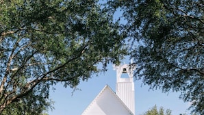 A white church with a bell tower, surrounded by trees and white chairs arranged for an event. - In Seaside – Nearby Pool & Beach – Emma Lou (Seaside)