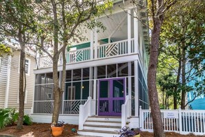 Une maison à deux étages avec un porche, une porte violette et une clôture blanche.