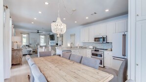 A modern kitchen with white cabinets, stainless steel appliances, and a wooden dining table. - In Seaside – Nearby Pool & Beach – Emma Lou (Seaside)